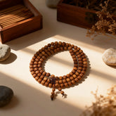 The multi-loop sandalwood mala in soft light, its overlapping circles creating shadows and light, symbolizing the spiral of growth and return.